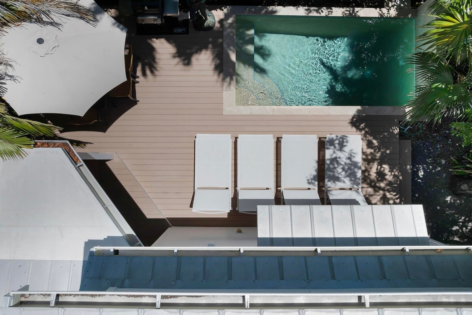 Overhead view of the pool, loungers, dining umbrella and grill on the deck