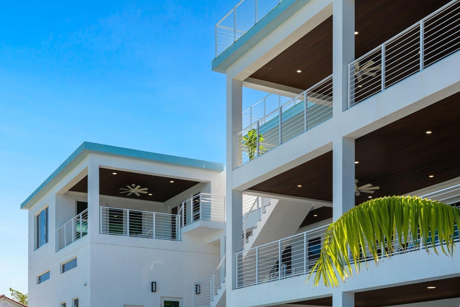 White exterior with stacked covered balconies and cable railings against a blue sky