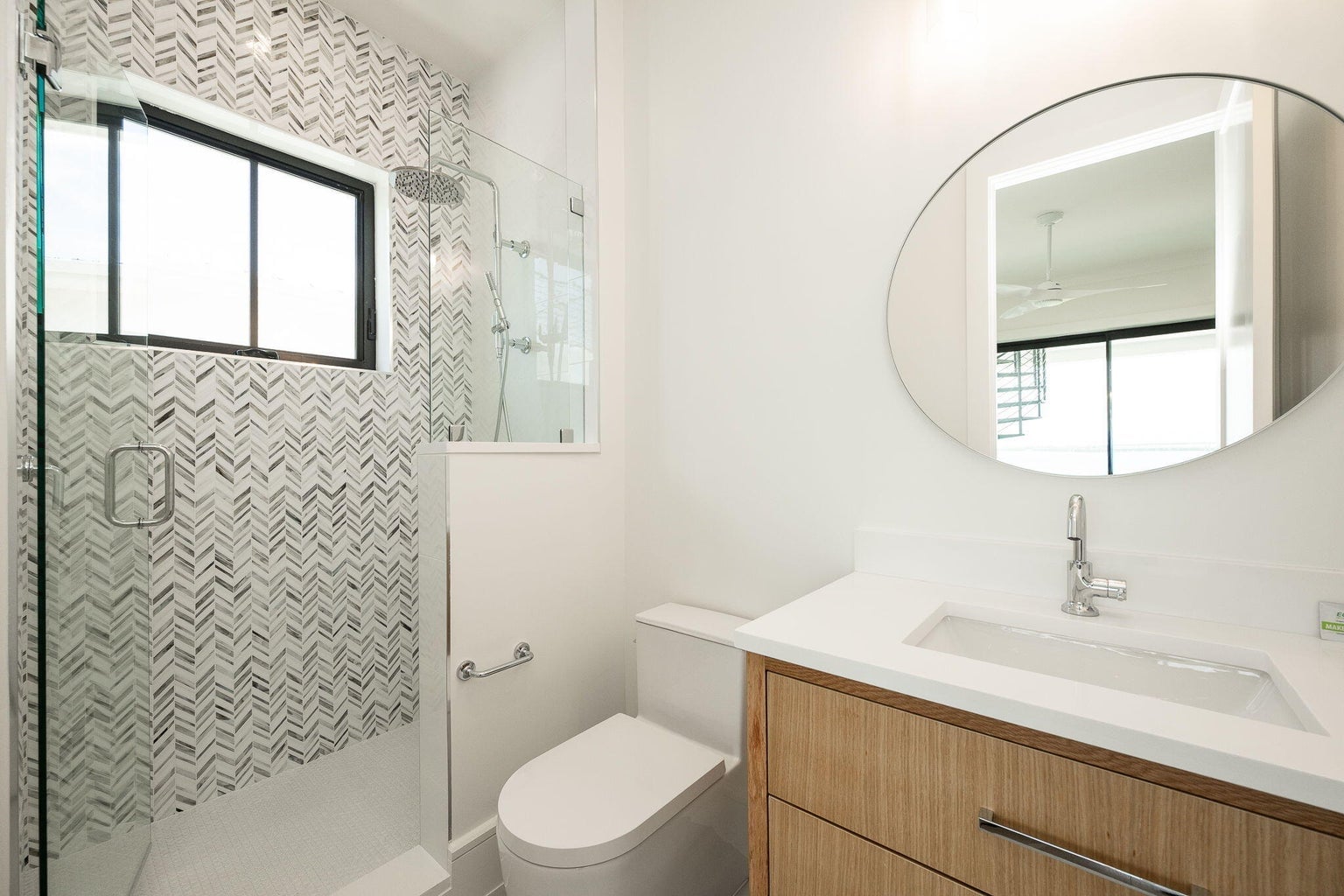 Bathroom with a chevron-tiled glass shower, an oval lit mirror and a wood vanity