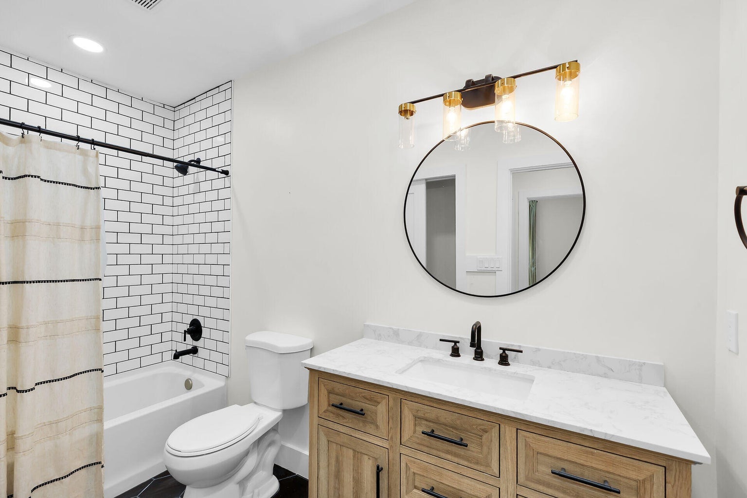 Bathroom with a wood vanity, round mirror and a tub with white subway tile
