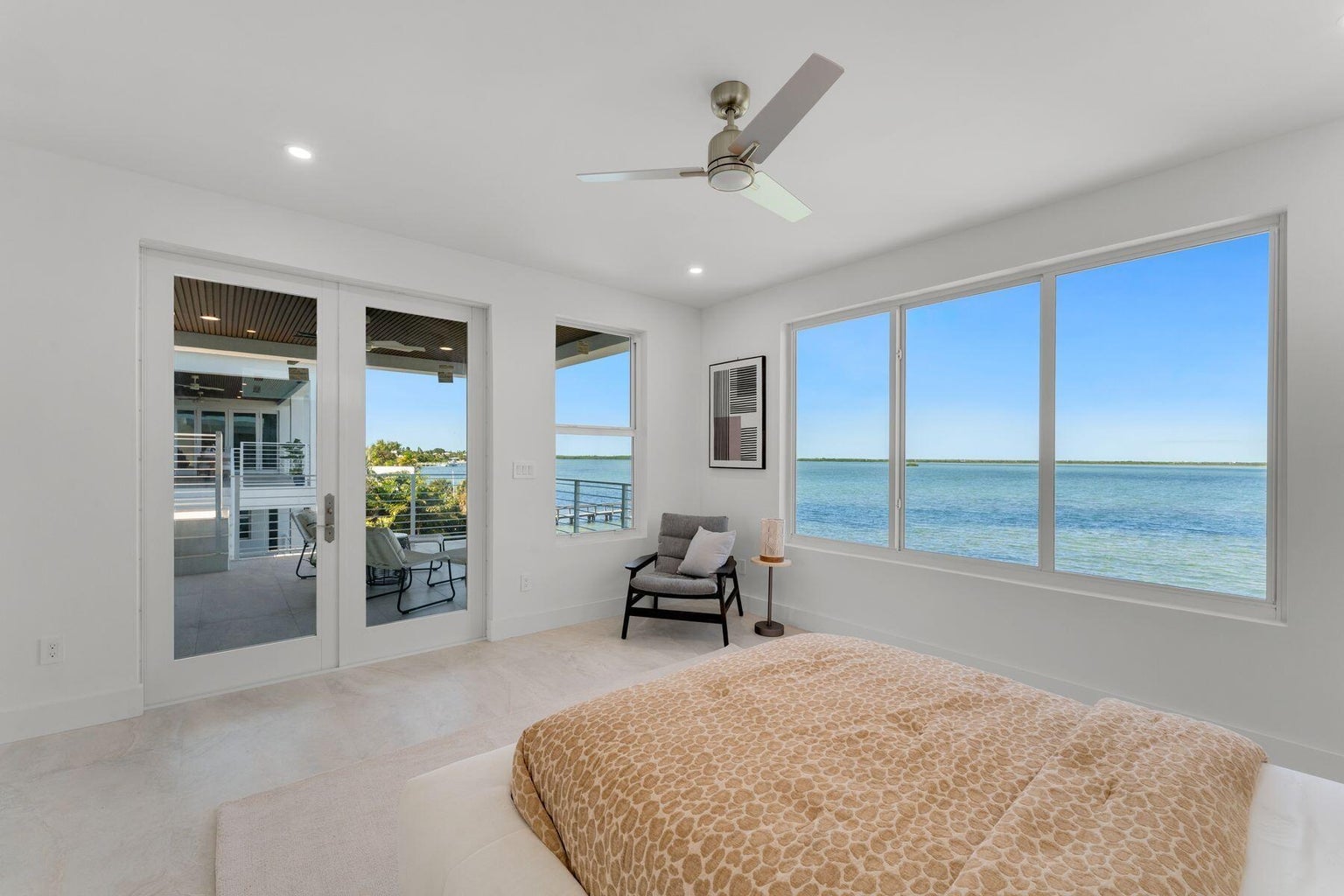 Bedroom with a wall of windows facing the water and French doors to a terrace