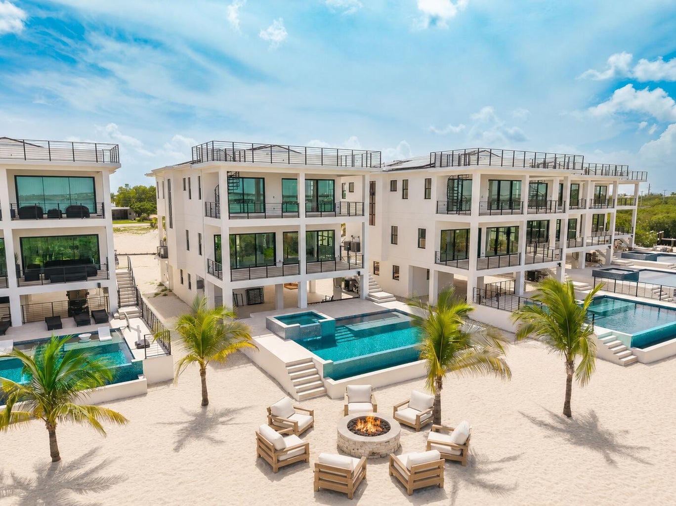 Three-story Seven Palms Cove residences with rooftop decks above private pools, palms and a fire-pit lounge on the sand