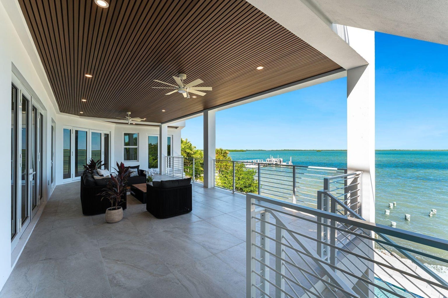 Covered terrace with wood-slat ceiling, ceiling fans and lounge seating overlooking the water