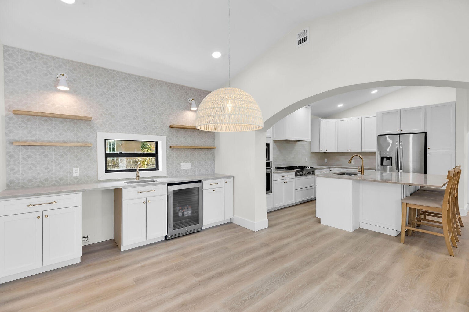 Open dining area with a woven pendant light and a wet bar, the kitchen and island through an arch