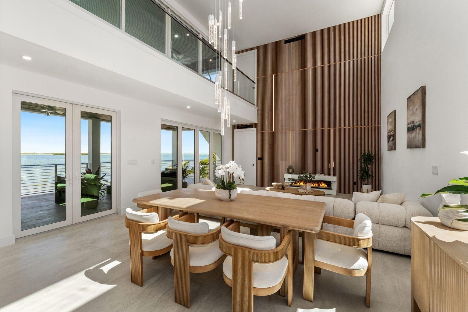 Dining table for eight beneath a pendant chandelier, with glass doors to a water-view terrace