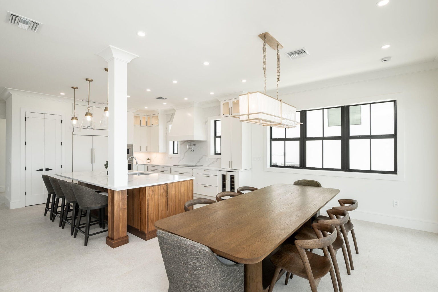 Walnut dining table for eight beneath a linear pendant, beside the kitchen island and its counter stools