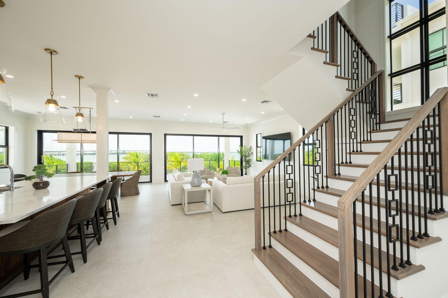 Open main level from the staircase, with a black-and-wood railing, the kitchen island and the living room's glass doors