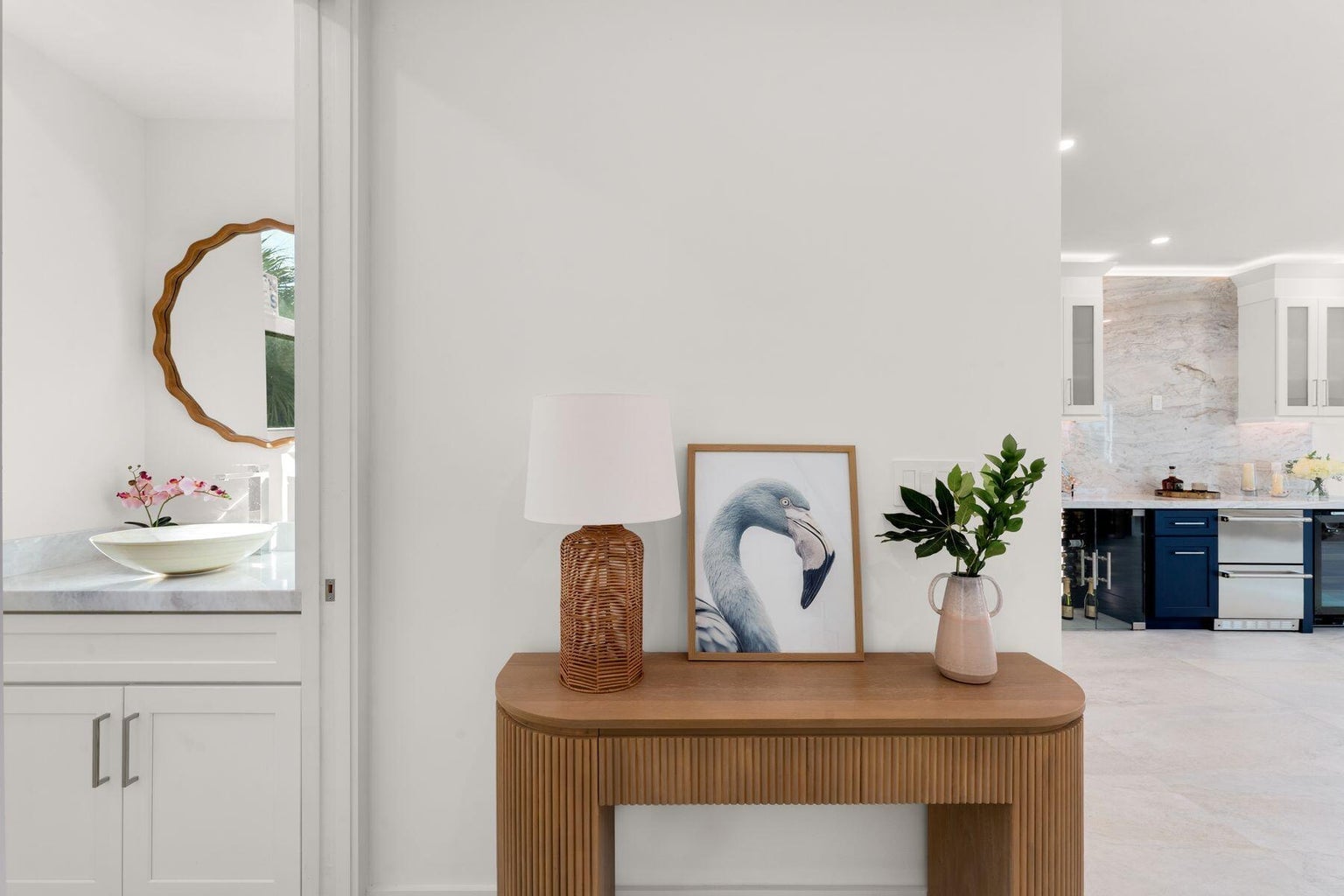 Hallway console with a lamp and flamingo print, the kitchen visible beyond