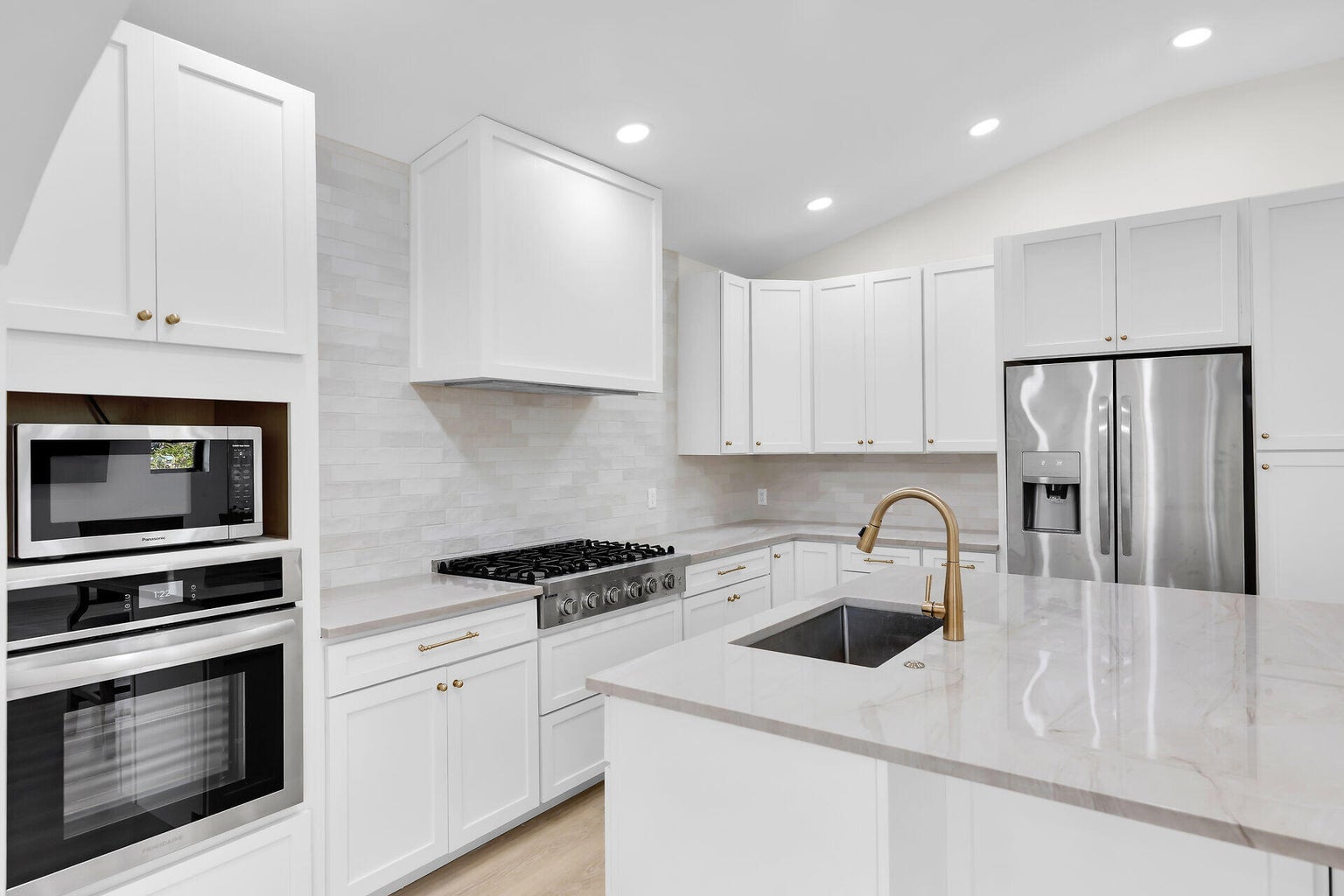 White kitchen with quartz counters, a gas range, stainless appliances and an island with a brass faucet
