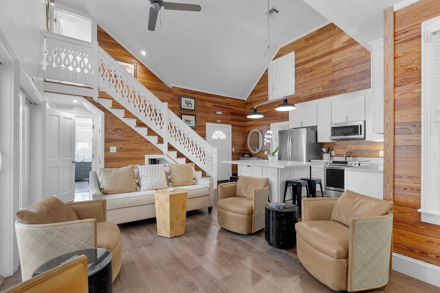 Vaulted living room with pine-paneled walls, a white gingerbread staircase and the kitchen beyond
