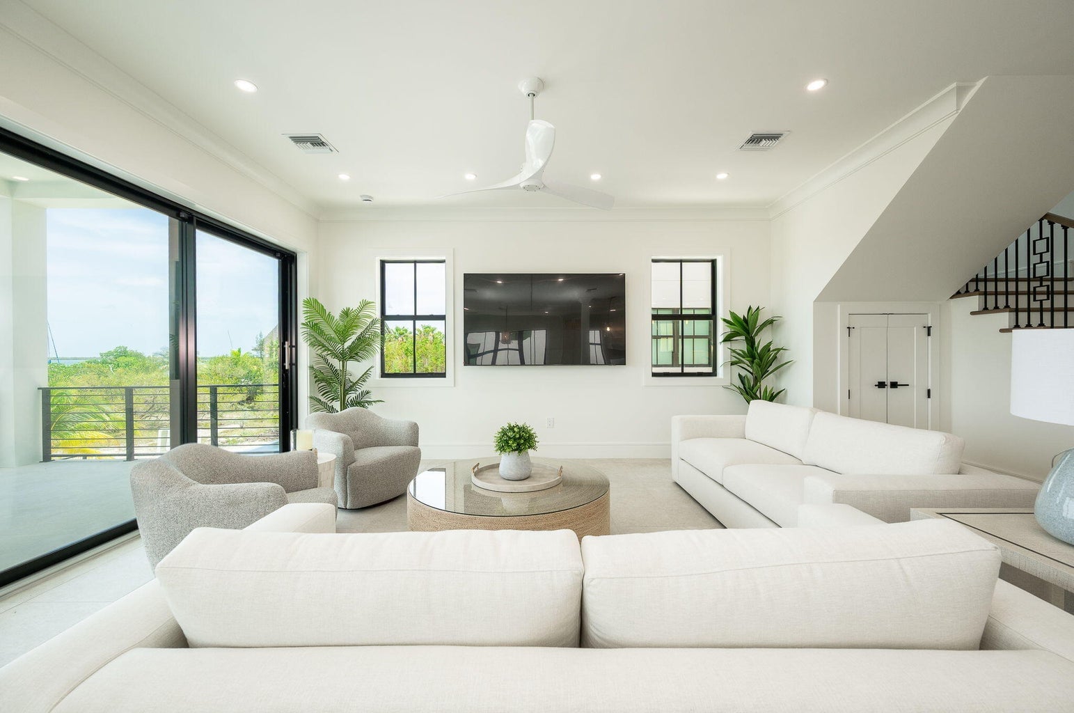 Living room with a white sectional, a wall-mounted TV between black-framed windows and sliding glass doors to a balcony