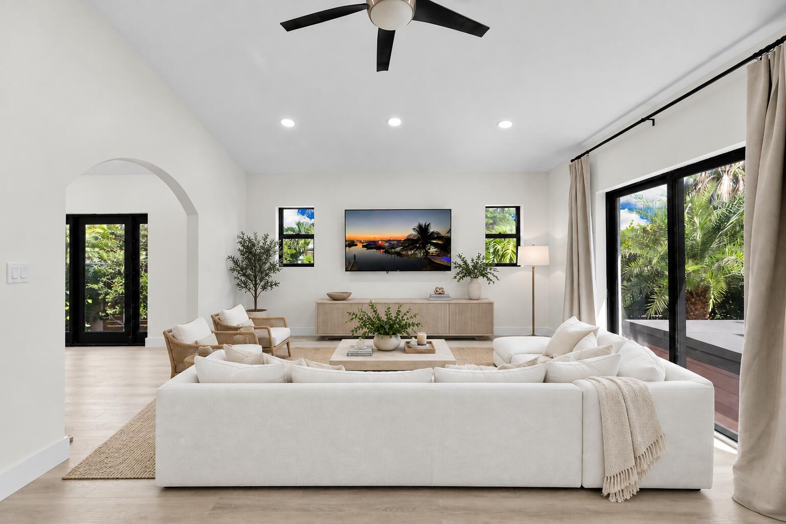 Living room with a vaulted ceiling, arched doorway, white sectional and sliding glass doors to the yard