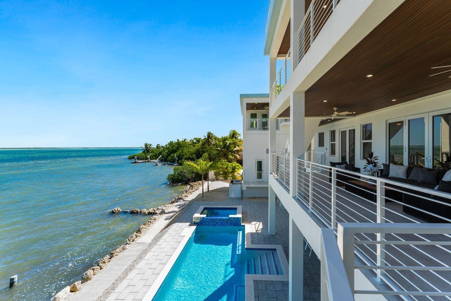 View from an upper terrace over the pool and spa to the open water and a palm-lined shoreline