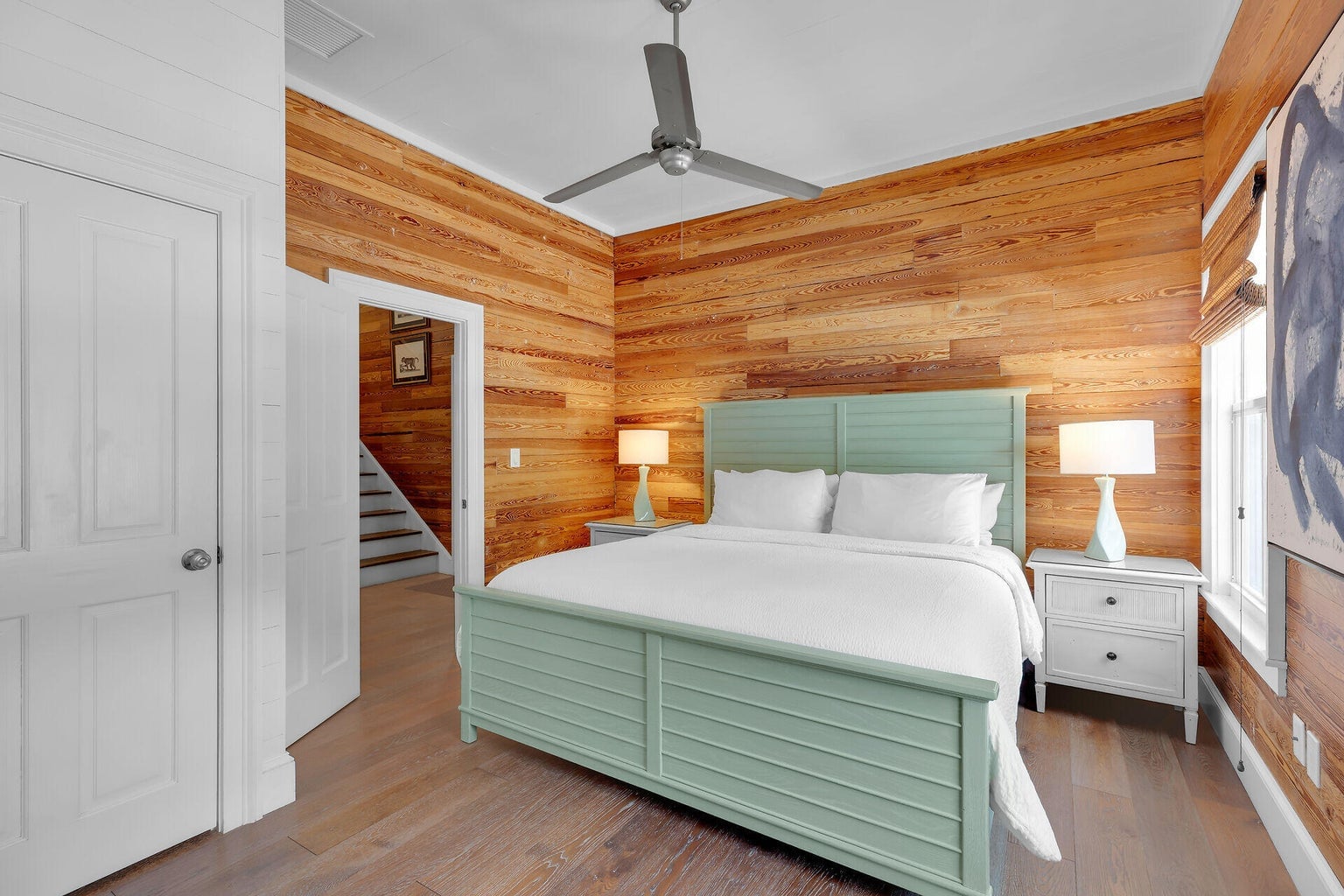 Bedroom with pine-paneled walls, a sage-green king bed and the staircase visible through the door
