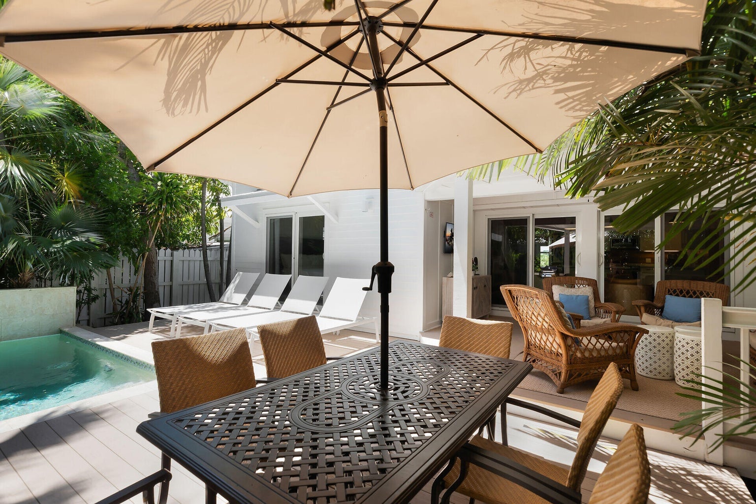 Dining table under a market umbrella beside the pool and a covered lanai with wicker chairs