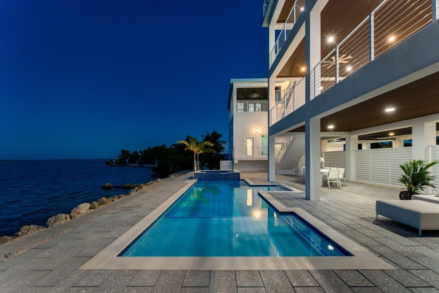 Pool and paver deck beside the seawall at dusk, with open water to the horizon