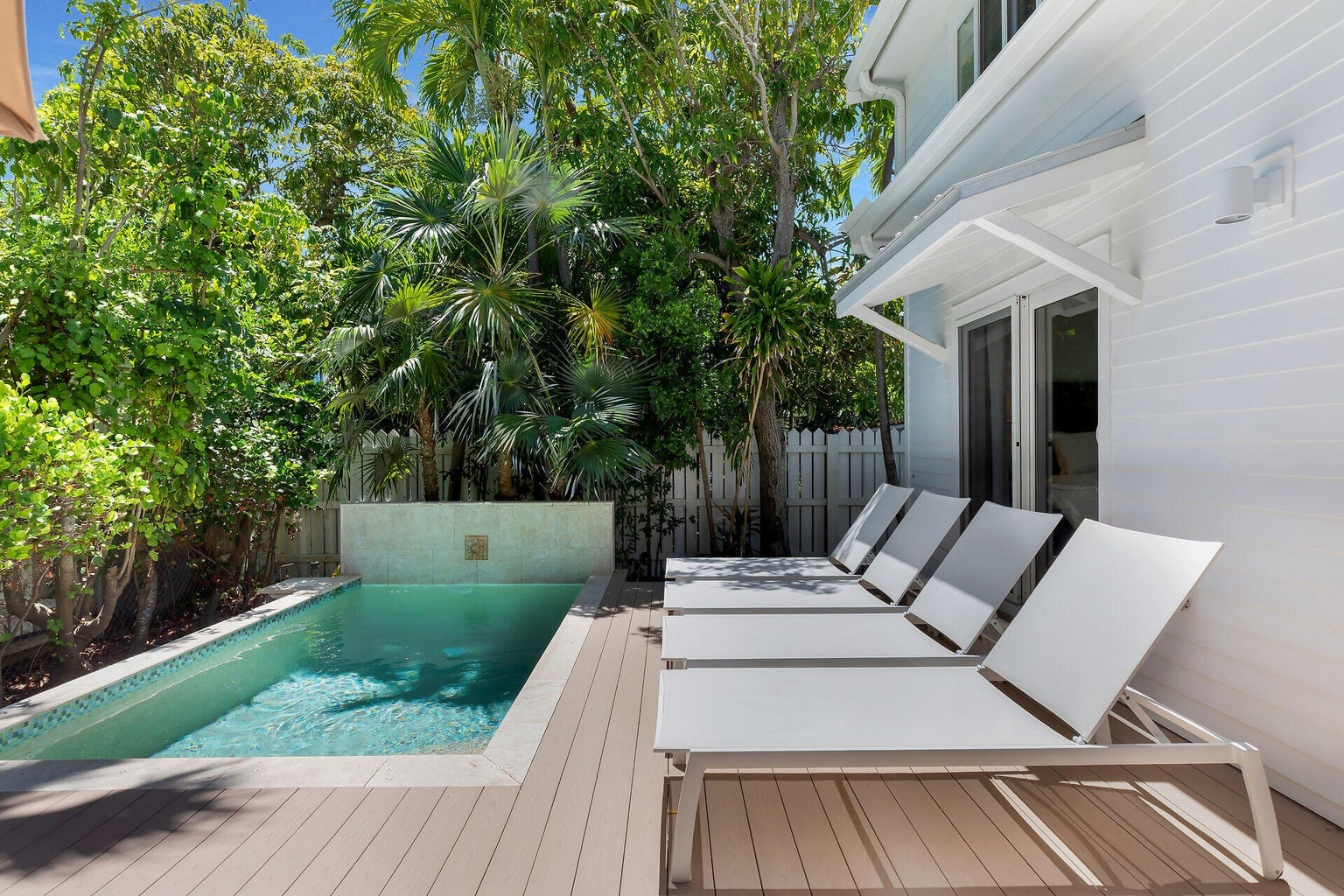 Pool with a stone water-feature wall, a composite deck and four loungers beside the house