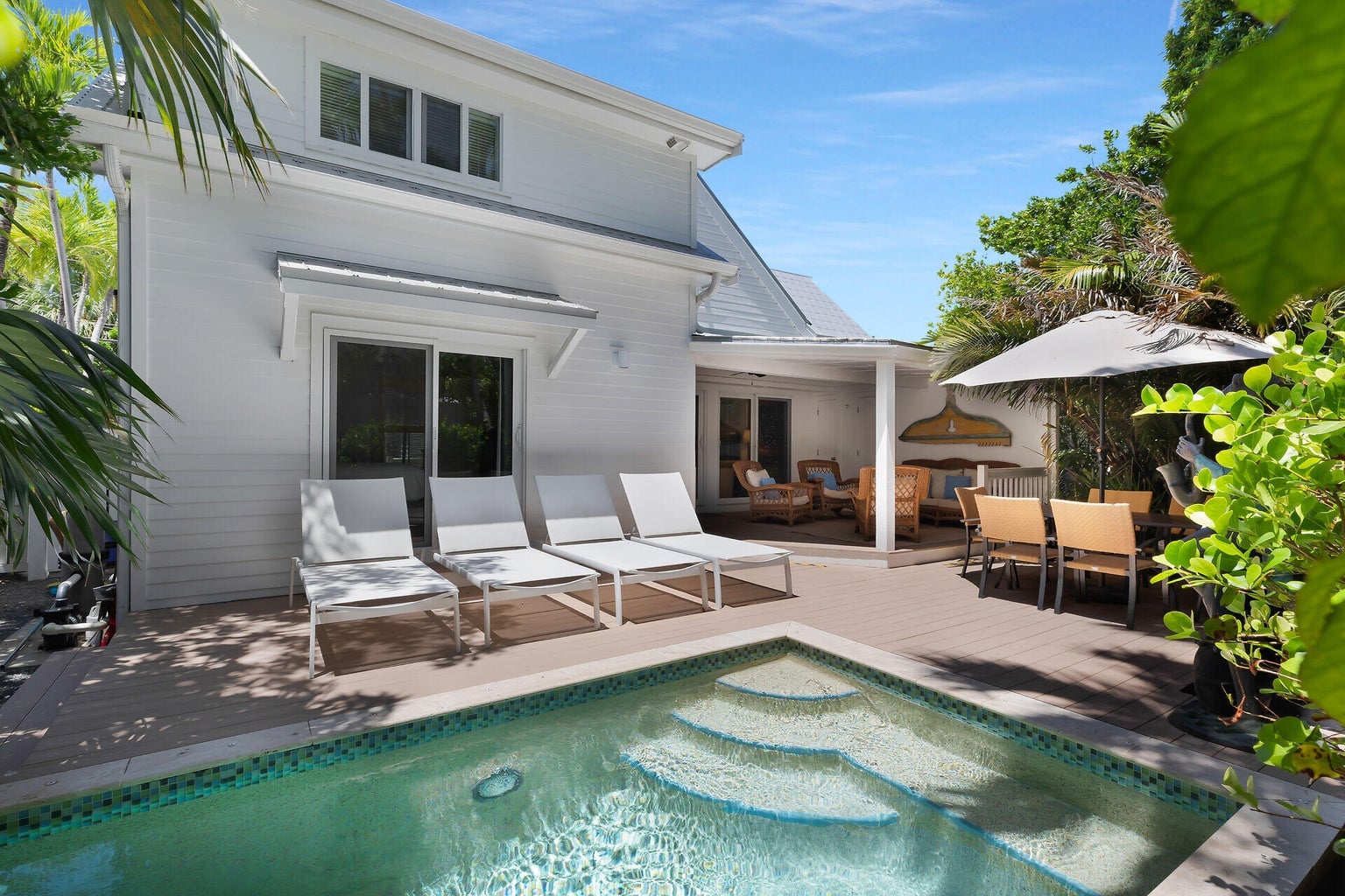 Plunge pool with tiled steps, four white loungers and a covered lanai with wicker seating