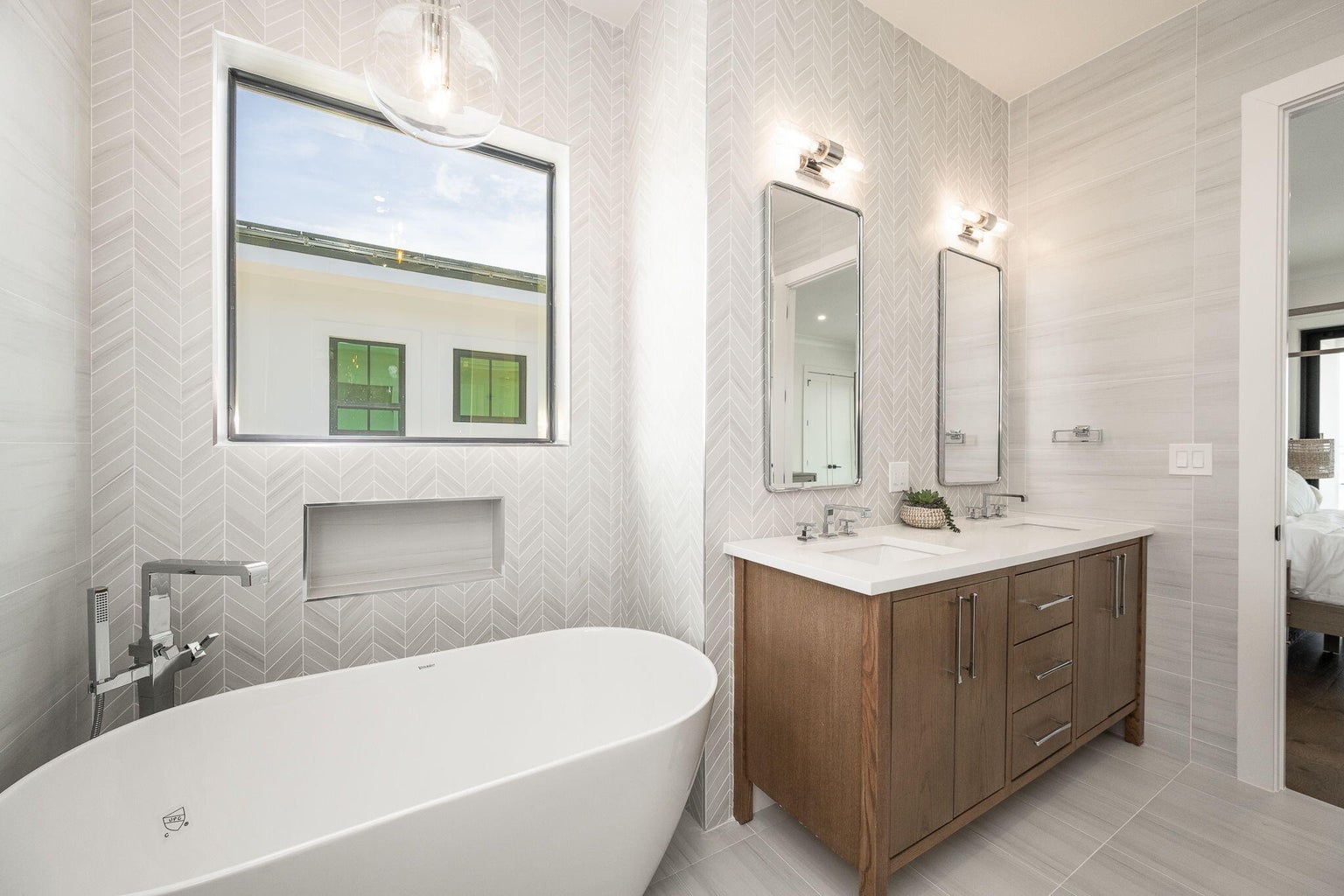 Bathroom with a freestanding soaking tub, a wood double vanity and herringbone wall tile