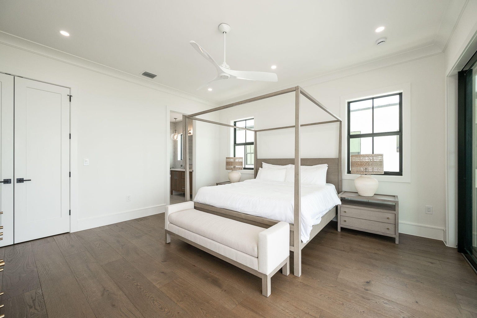 Bedroom with a four-poster bed, an upholstered bench, wood floors and white double doors