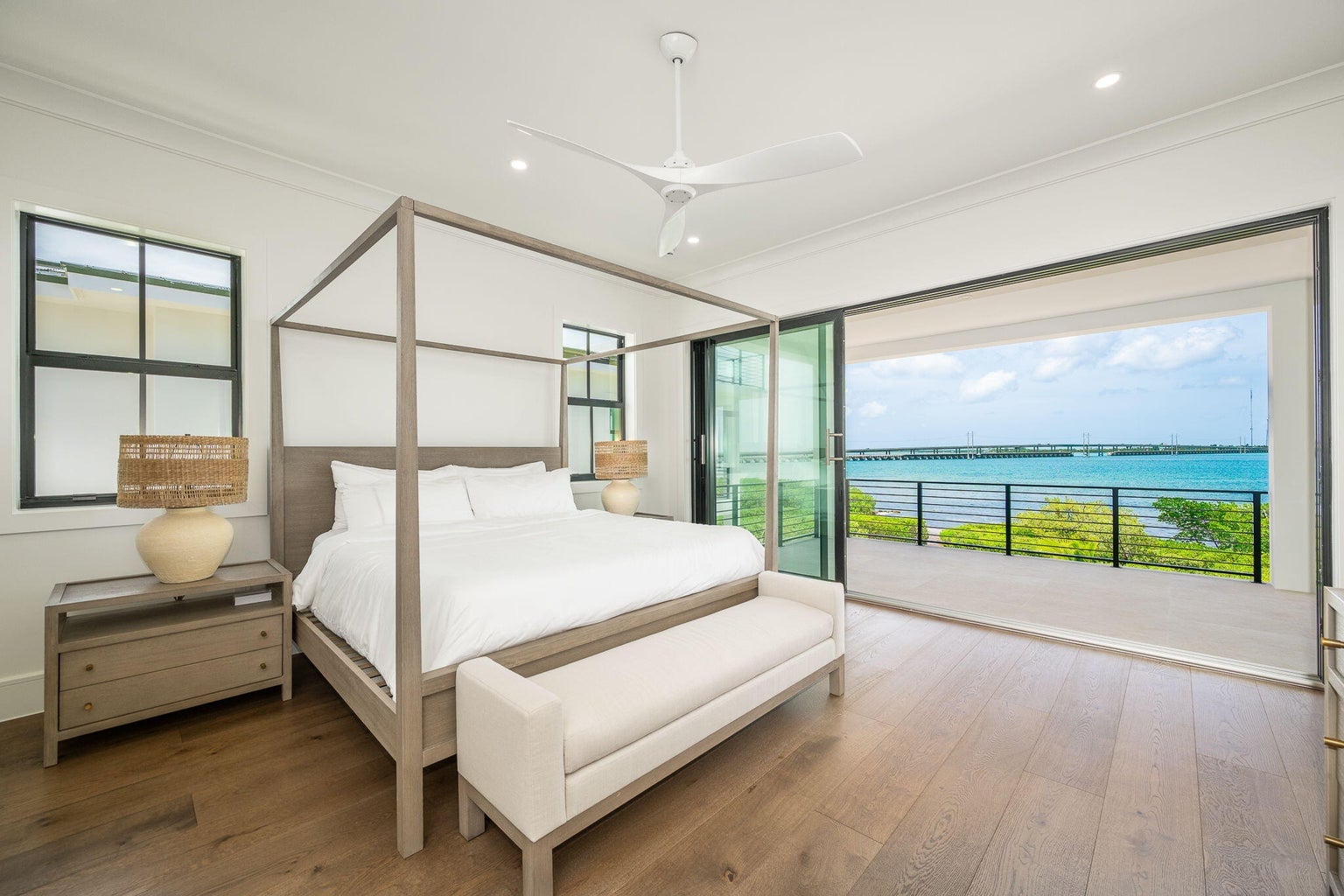 Bedroom with a four-poster bed and wood floors, its glass doors opened to a veranda over turquoise water