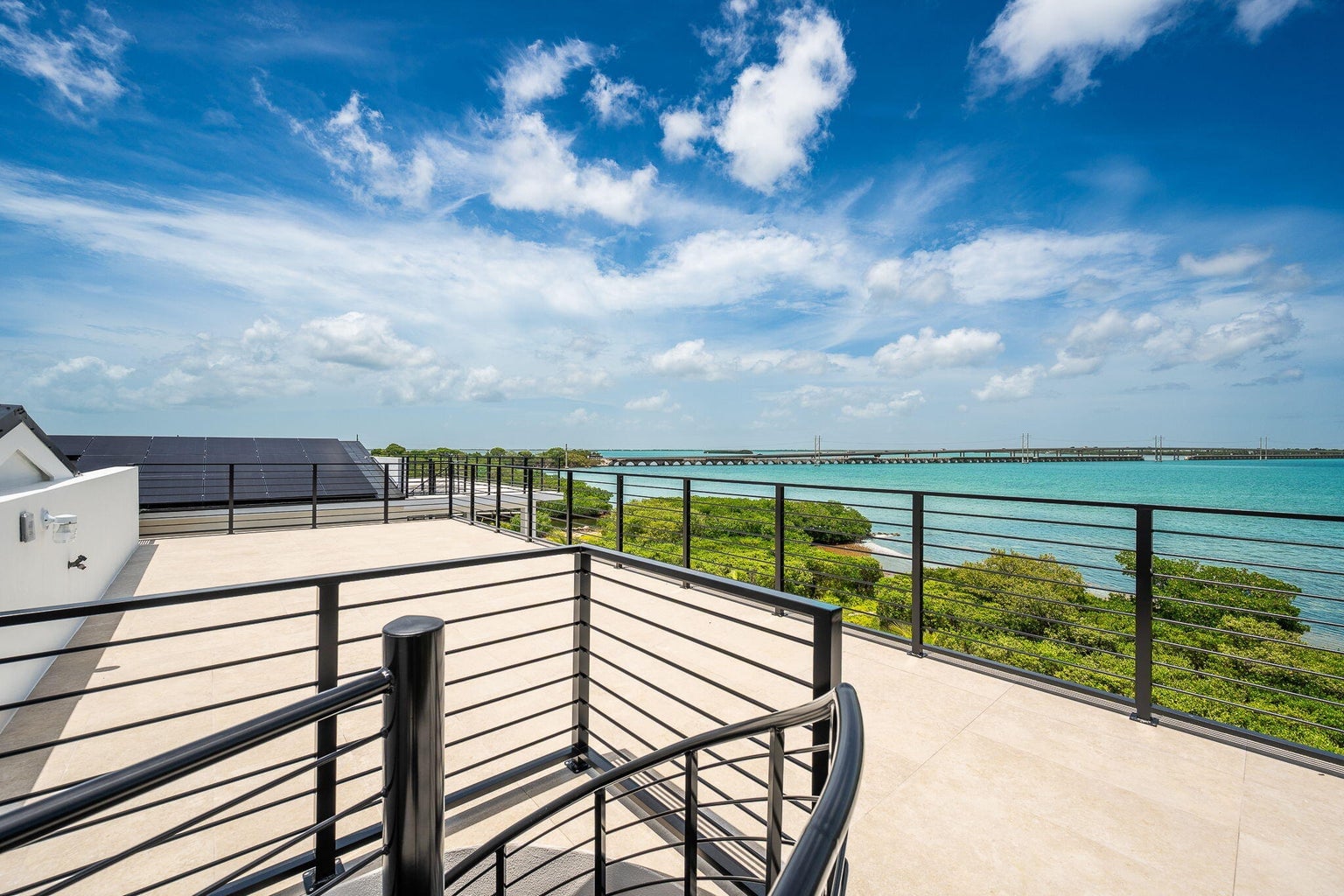 Rooftop deck with a curved black railing above mangroves, turquoise water and a long bridge