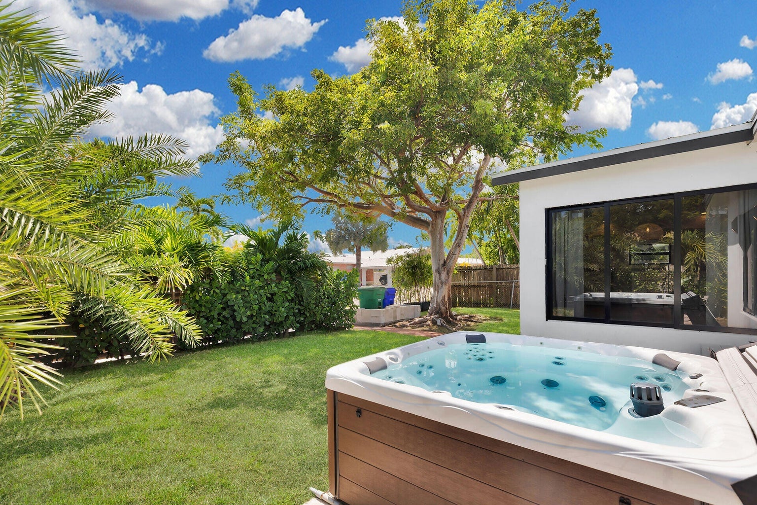 Lawn and shade tree beside the house, with a hot tub on a wood deck and tropical hedges