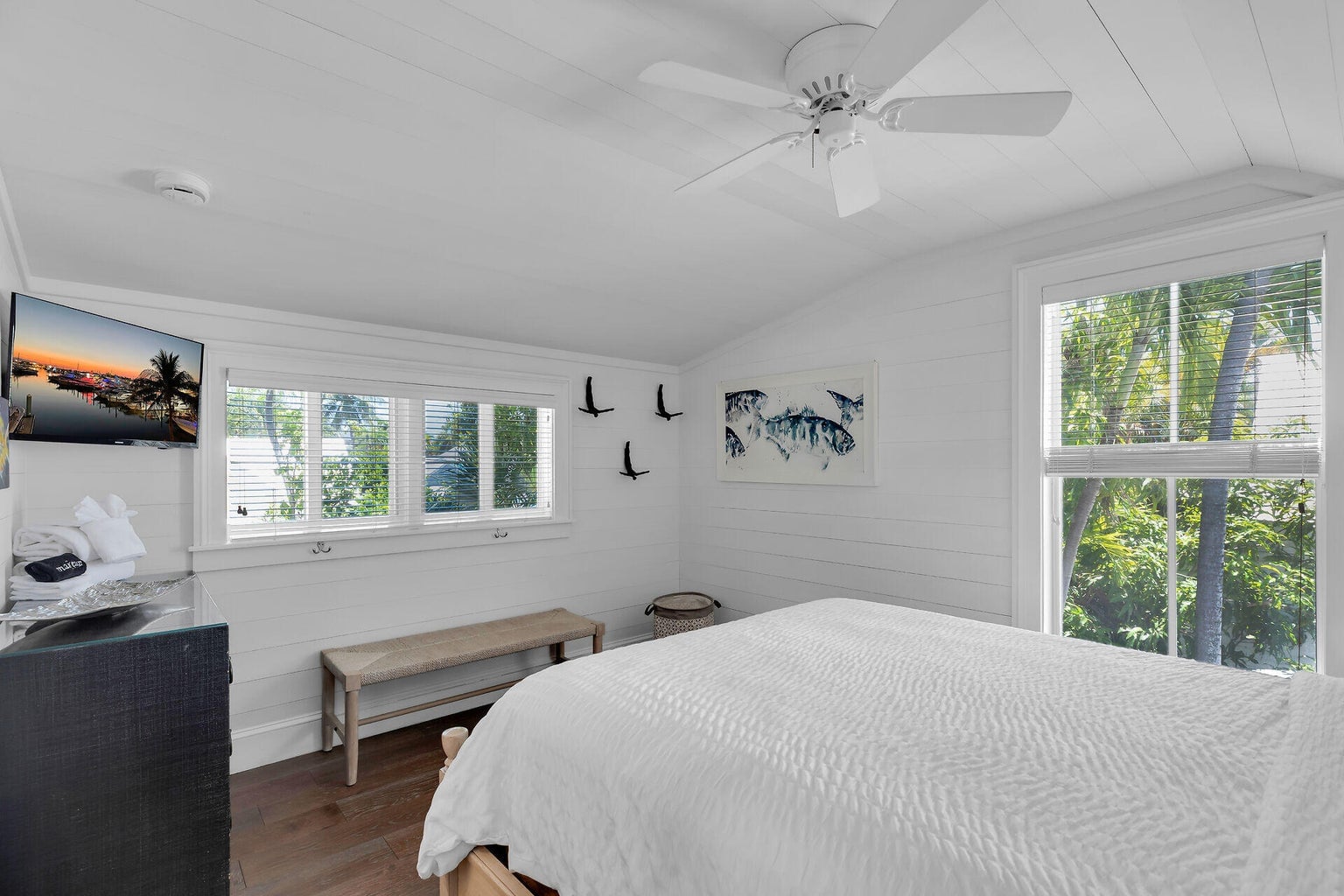 Upstairs bedroom with a vaulted white ceiling, windows into the palms and a wall-mounted TV