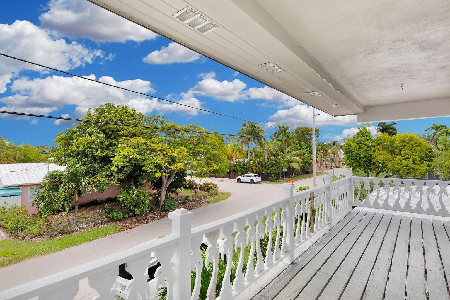 Covered upstairs porch with a white railing looking over the palm-lined street